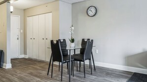 Un coin repas avec une table en verre et des chaises noires, une porte blanche et une horloge au mur.