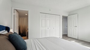 Een slaapkamer met een groot bed, twee deuren en een zichtbare badkamer.