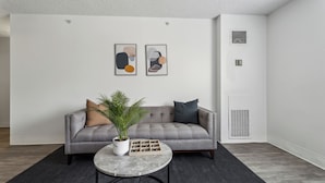 Een moderne woonkamer met een grijze bank, een kleine ronde tafel en abstracte wanddecoratie.