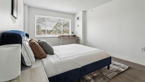 Een slaapkamer met een bed, nachtkastje, lamp en raam.