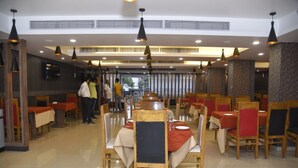 Un restaurant avec de nombreuses tables et chaises, dont certaines sont recouvertes de nappes rouges.