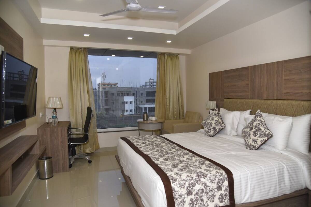 A hotel room with a bed, a desk, a chair, a TV, and a window with curtains.