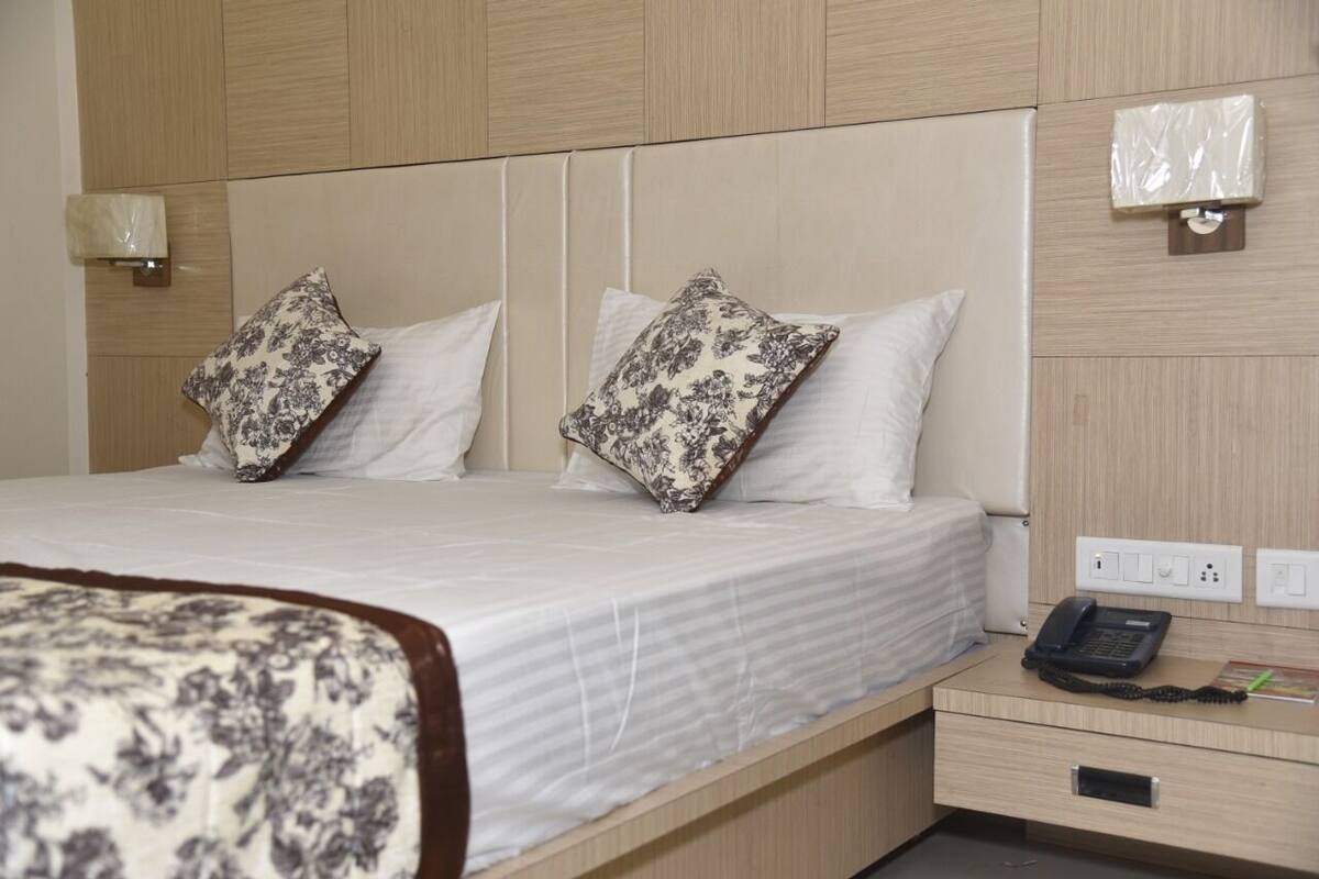 A hotel room with a bed, two pillows, a bedside table with a phone, and a wall-mounted light.