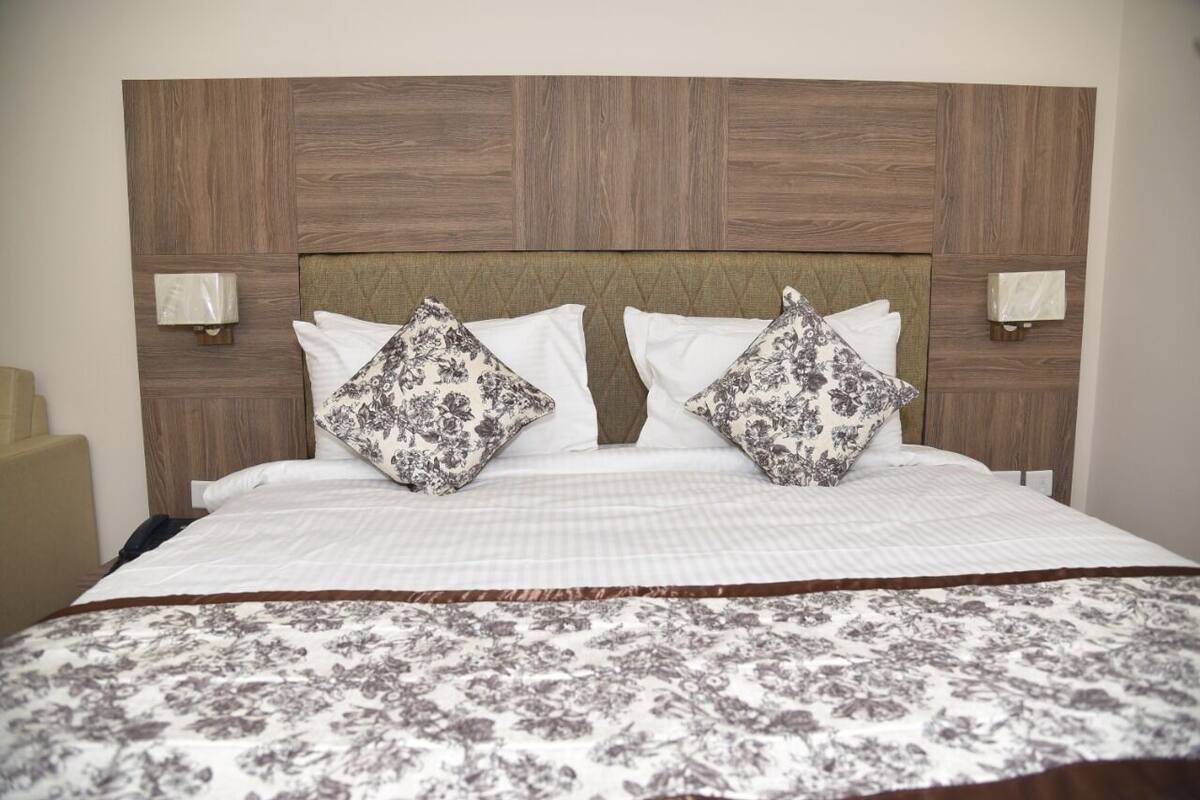 A hotel room with a wooden headboard, two bedside lamps, a floral-patterned bedspread, and a matching pillow.