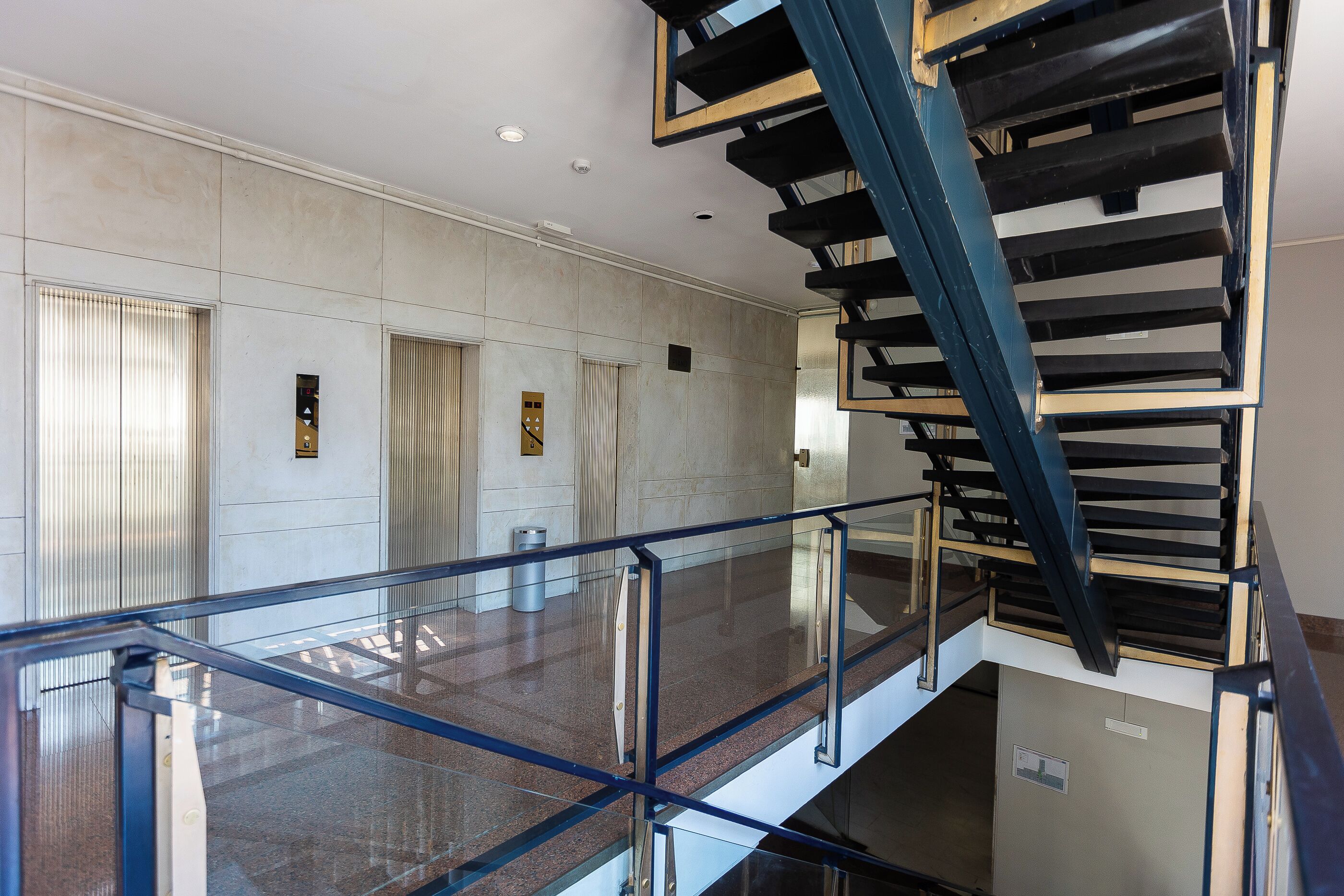 Un intérieur moderne avec une balustrade en verre, un escalier et un sol carrelé aux lignes épurées.