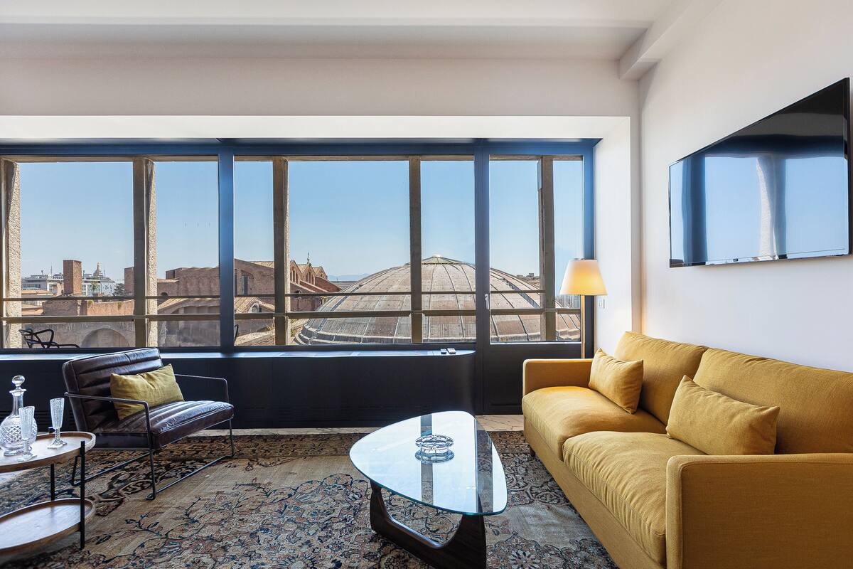 Ein modernes Wohnzimmer mit einer Couch, einem Glastisch und Blick auf eine Skyline durch große Fenster.