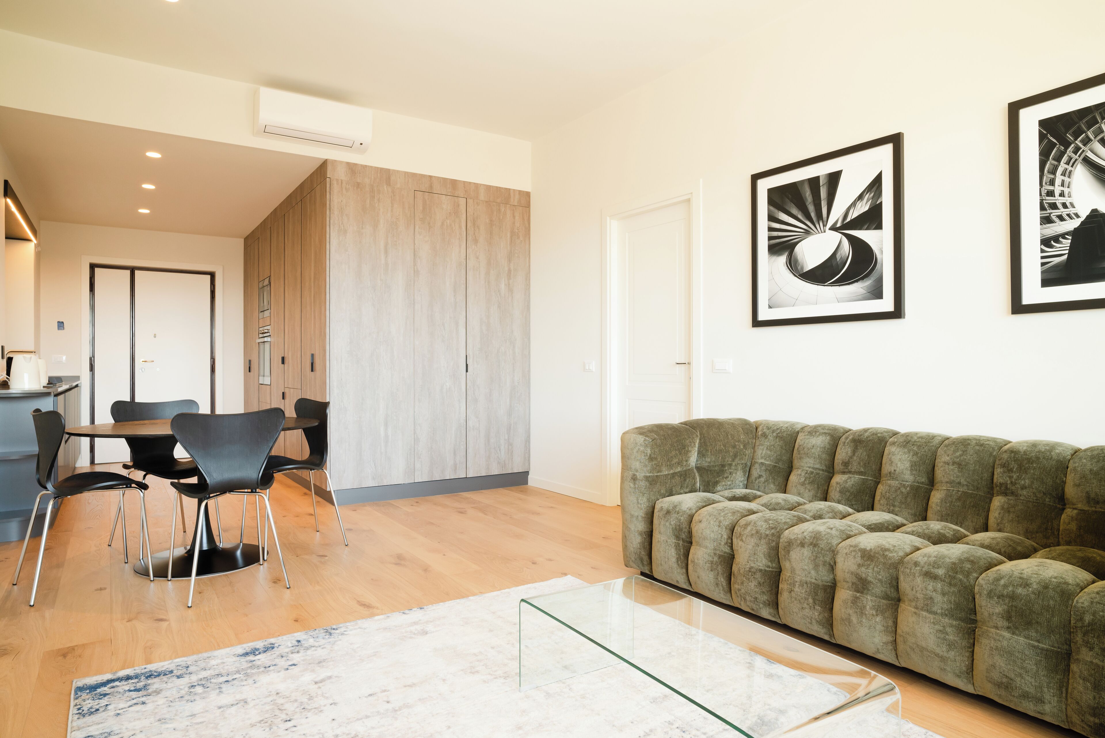 A modern living room with a sofa, a glass coffee table, a dining table with chairs, and framed artwork on the wall.