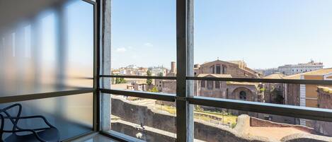 A room with large windows overlooking ancient ruins and modern buildings.