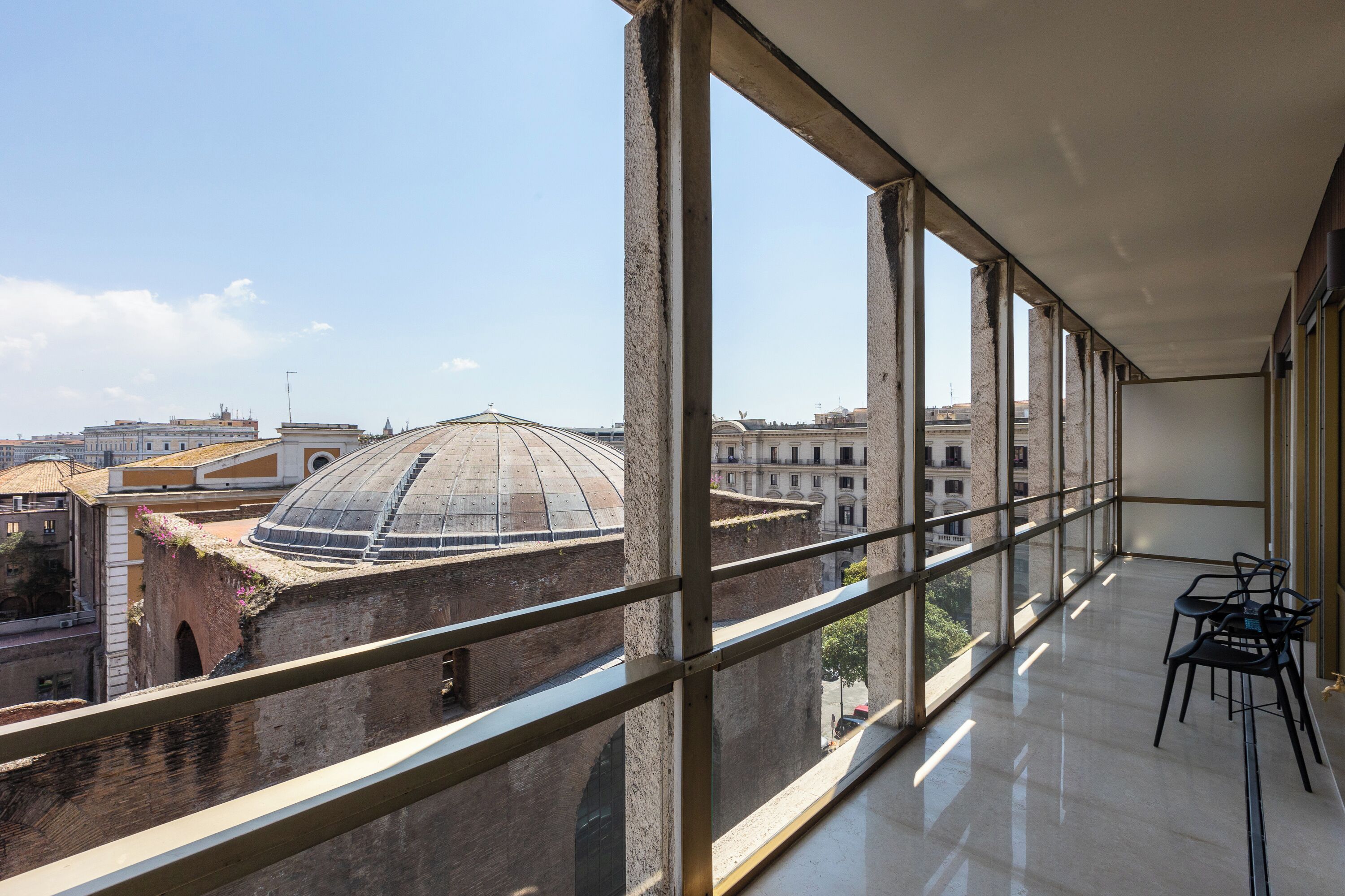 A high-rise room with large windows offering a view of historic buildings and a dome.