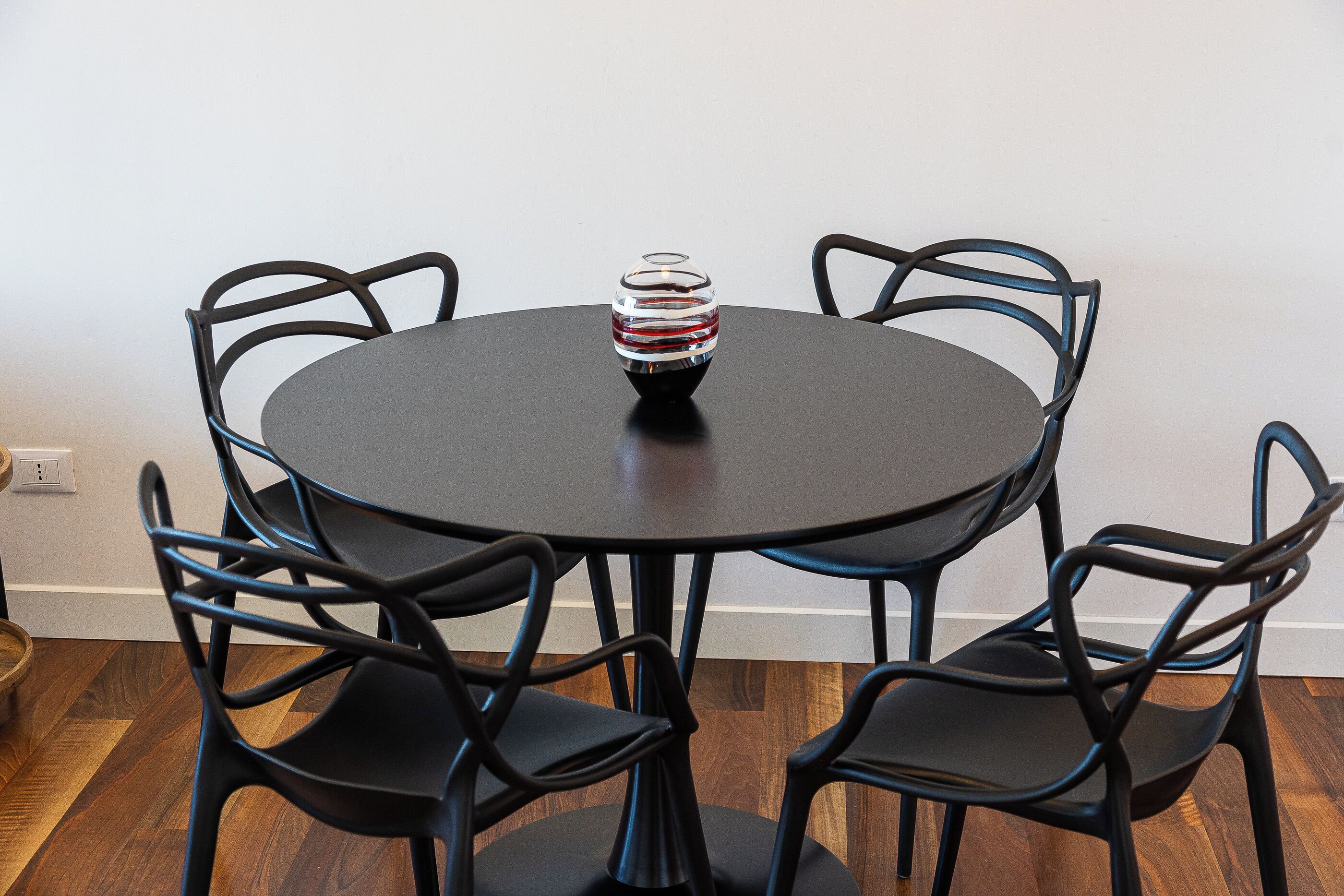 A round table with six black chairs around it, a decorative glass vase in the center, and a wooden floor.