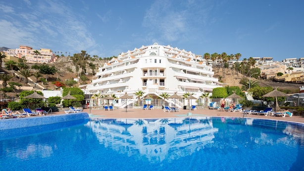 A large hotel with a swimming pool, multiple balconies, and a hillside view.
