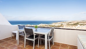 A balcony with a table and chairs, overlooking a coastal cityscape.