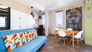 A modern kitchen with white cabinets, a blue sofa, and a dining area with a wooden table and white chairs.