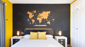 A hotel room with a large bed, two bedside tables with lamps, a world map on the wall, and a wardrobe.