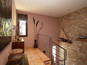 Eine Treppe mit Metallgeländer, eine Wand mit Steinmuster und ein kleines Regal mit einem Modellschiff.