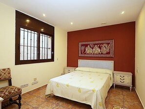 Ein Schlafzimmer mit einem Bett, zwei Nachttischen, einem Sessel, einem Fenster mit Gitter und einer Wanddekoration.