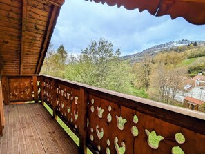Un balcon en bois offrant une vue sur une vallée et des bâtiments éloignés.