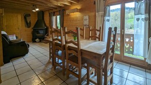 A cozy cabin interior with a wooden dining table, chairs, a fireplace, and large windows offering a view of the outdoors. - Spacious chalet in La Bresse, perfect for families and friends (La Bresse)