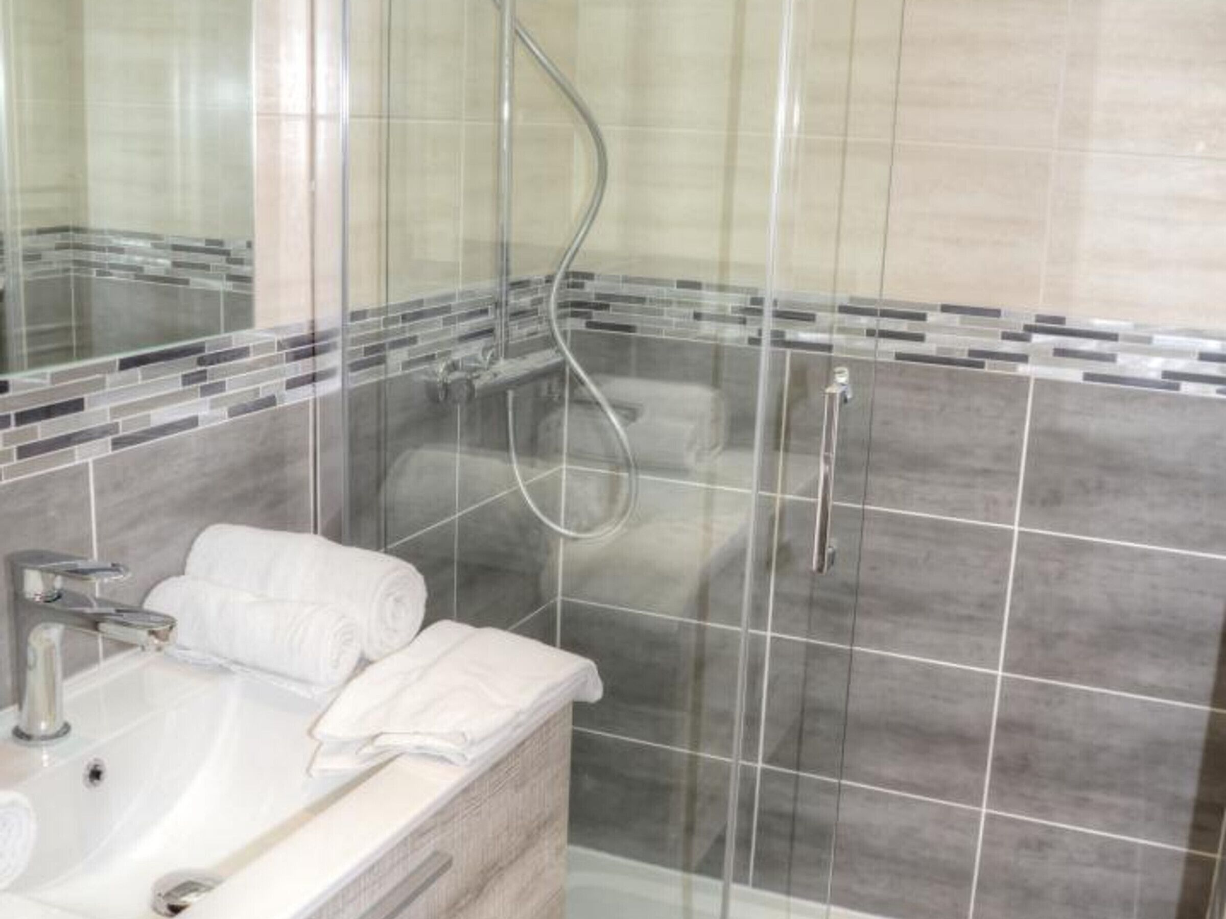 Een moderne badkamer met een glazen douchecabine, een witte wastafel en een handdoekhouder.