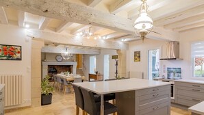 Une cuisine spacieuse avec un îlot central, un coin repas avec des chaises et une horloge visible au mur.