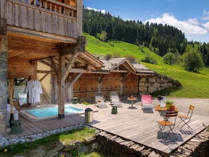 Una cabaña de madera con hidromasaje, mobiliario exterior y vistas a una ladera verde.