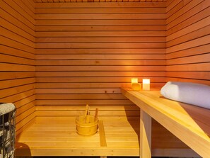 A wooden sauna with a bench, two lit candles, and a wooden bucket. - 5★ Chalet with spa, sauna & hammam for 15 people, close to slopes (La Clusaz)