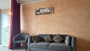 Ein modernes Wohnzimmer mit einem grauen Sofa, gemusterten Kissen, einem roten Vorhang und einem an der Wand befestigten Kunstwerk.