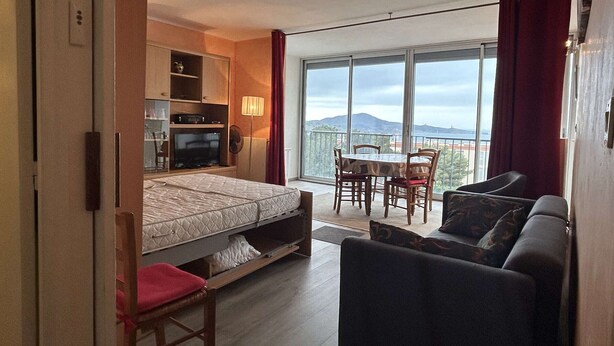 Ein Schlafzimmer mit Bett, Fernseher, Schreibtisch und einem Balkon mit Tisch und Stühlen.