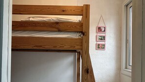 Ein Stockbett mit Holzrahmen und weißer Bettwäsche. Rechts an der Wand hängen drei kleine, rosa Bilderrahmen.