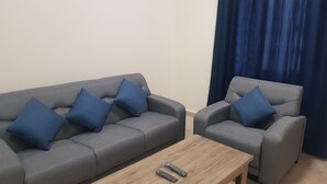 Ein Wohnzimmer mit zwei grauen Sofas, jedes mit einem blauen Kissen, und einem Holztisch mit zwei Fernbedienungen.