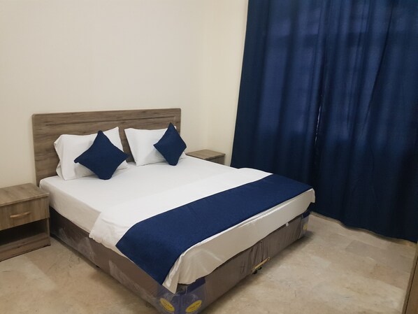 A bed with a wooden headboard, white and blue bedding, and a blue curtain. - Today House Suites 2 (Salalah)