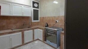 Eine Küche mit weißen Schränken, einem schwarzen Kühlschrank, einem Herd und einem Deckenventilator.