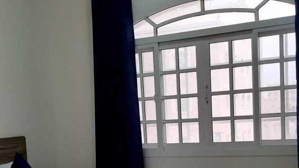 Ein Schlafzimmer mit Bett, einem Fenster mit Vorhängen und Blick auf Gebäude.
