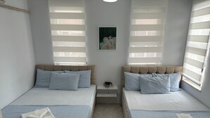 A twin room with two beds, each with a headboard, a small bedside table, and a window with blinds. - Avşa Çakır Apart (Marmara)