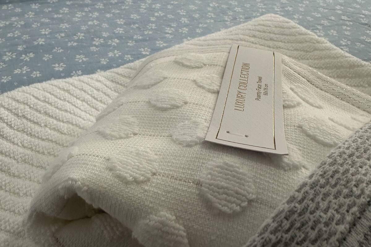 A neatly made bed with a blue floral bedspread and a white blanket with a label reading "Luxury Collection."