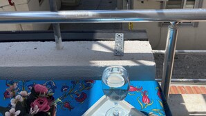 A balcony with a table set for two, featuring a glass of water, a cup of coffee, and a floral arrangement. - Avşa Çakır Apart (Marmara)