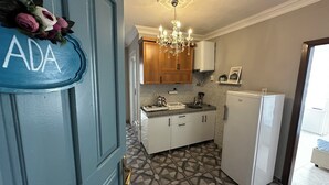 A kitchen with a blue door, a chandelier, wooden cabinets, a white refrigerator, and patterned floor tiles. - Avşa Çakır Apart (Marmara)