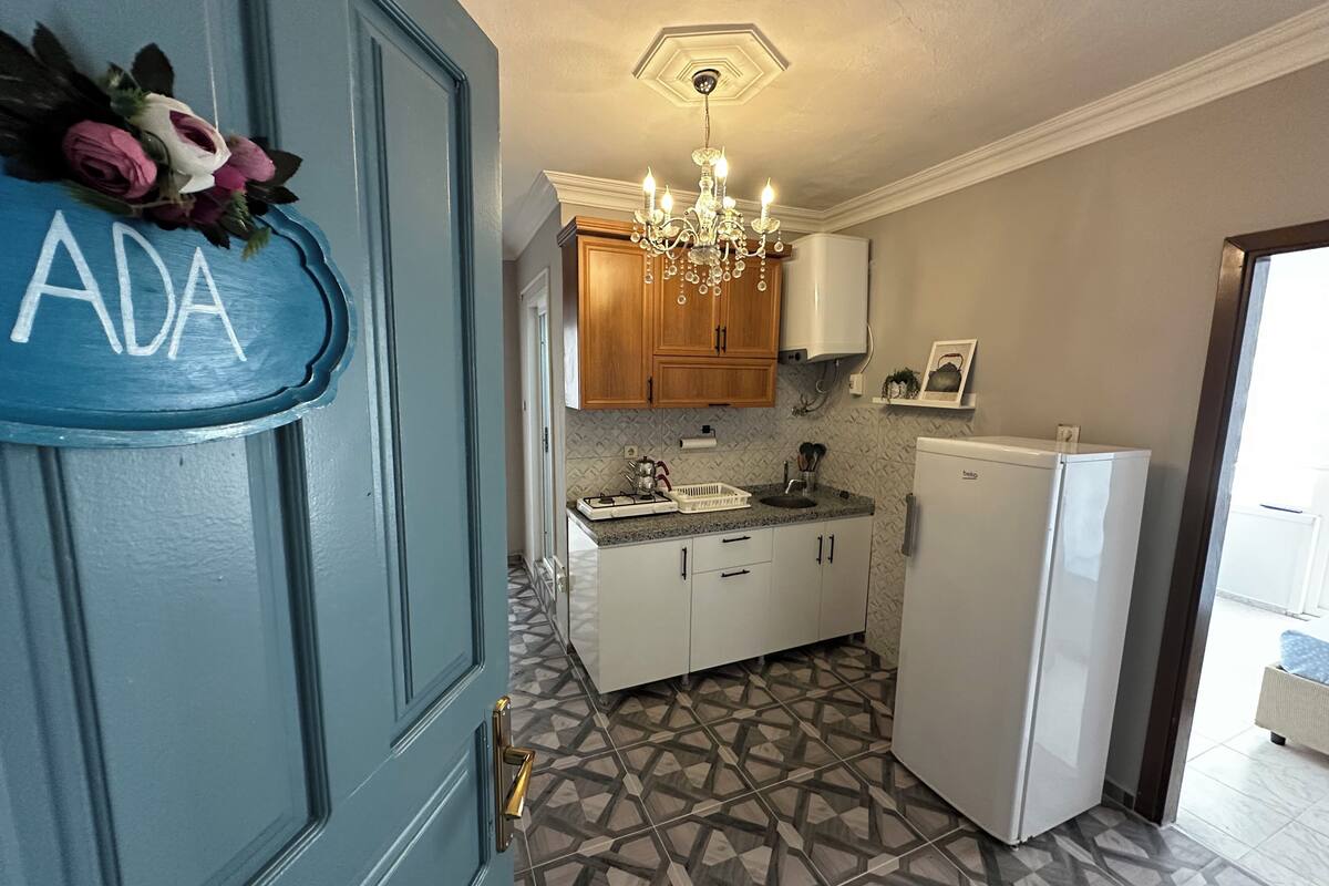 A kitchen with a blue door, a chandelier, wooden cabinets, a white refrigerator, and patterned floor tiles.