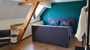 A bedroom with a sloped ceiling, a bed with floral bedding, a chair, and a coat rack. - B&B Catharinenburg (Melissant)
