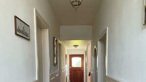 A hallway with white wainscoting, a wooden door at the end, and a chandelier. - B&B Catharinenburg (Melissant)