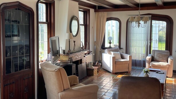 A spacious living room with a fireplace, comfortable seating, and large windows offering natural light. - B&B Catharinenburg (Melissant)