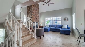 A spacious living room with a stone accent wall, a blue sectional sofa, and a staircase with white balusters. - Steps to Beach & Bay | A/C, Patio & 4 Park Spots (San Diego)