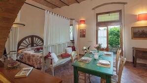 A cozy room with a bed, a dining table set for two, and a window with a view of greenery.