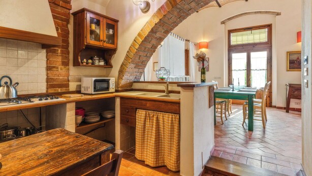 A kitchen with a brick archway, wooden cabinets, a microwave, and a dining area with a table and chairs.