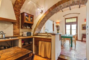 A kitchen with a brick archway, wooden cabinets, a microwave, and a dining area with a table and chairs.