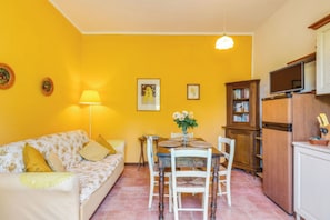 A compact living space with a sofa, dining table, chairs, a lamp, a bookshelf, and a television.