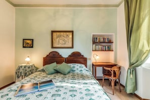 Un dormitorio con cama, escritorio, silla, estantería y ventana con cortinas.