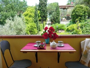 Un balcón con una mesa preparada para tomar té, rodeado de follaje y vista a un edificio.