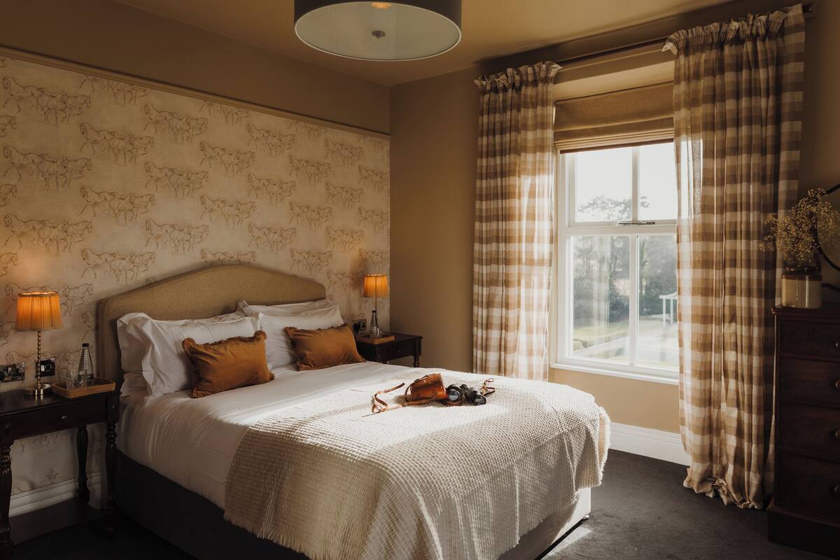 Un dormitorio con una cama grande, dos mesitas de noche con lámparas, una ventana con cortinas y una pared con estampado floral.