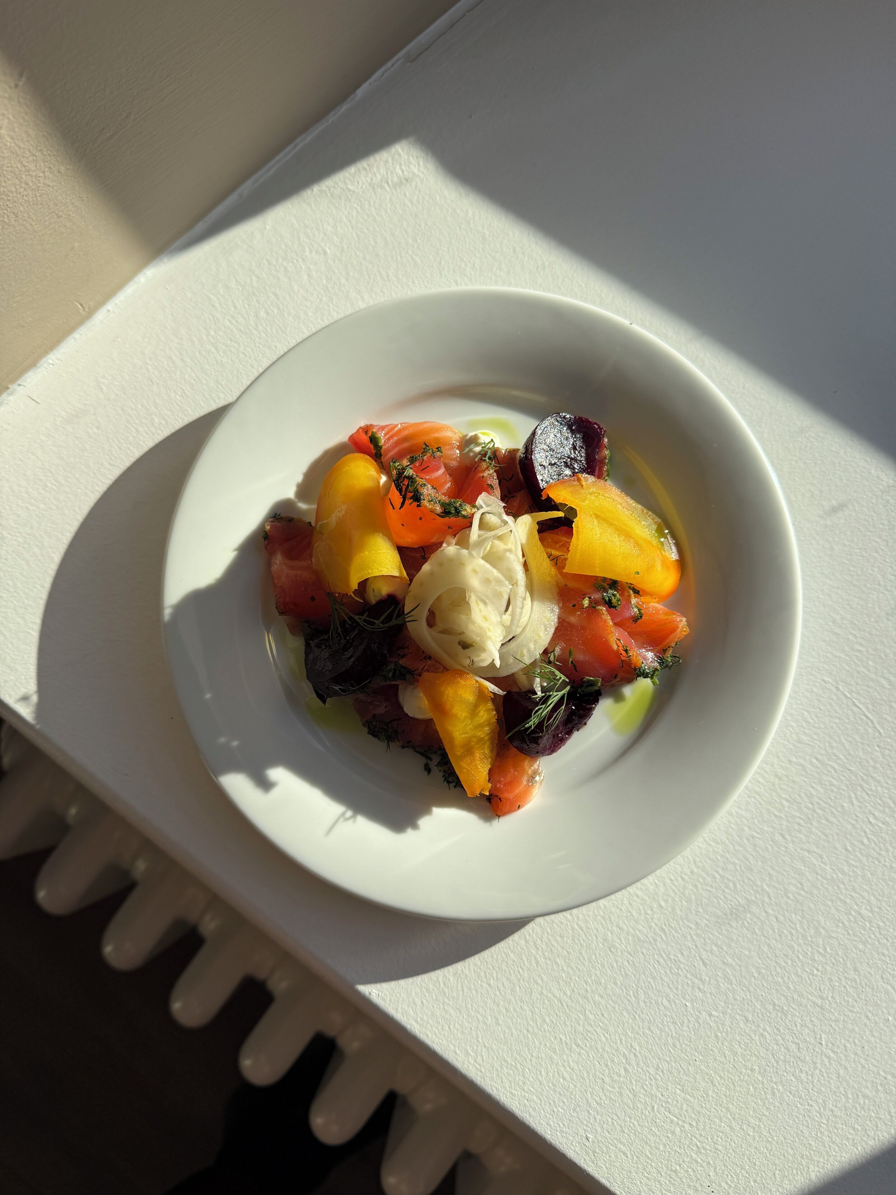 A white plate with a salad on a white table.